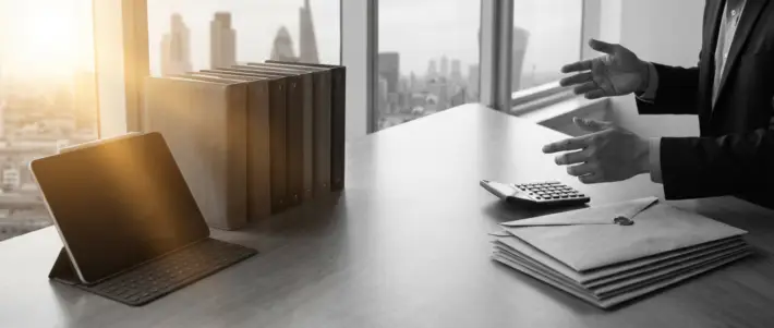 a professional in a suit discussing ofccp compliance budgeting with a tablet, calculator, and folders on a modern office desk overlooking a city.
