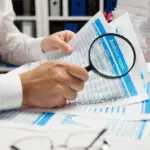 man's hands analyzing financial data on an analysis report with a magnifying glass