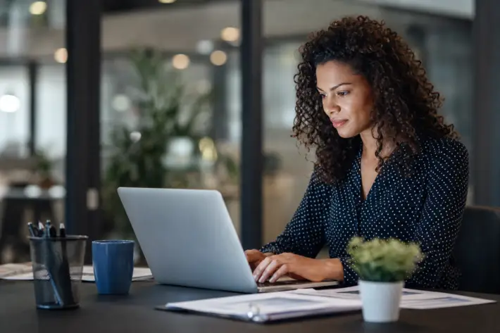 woman with curly hair typing on laptop, reviewing ofccp holiday job postings.