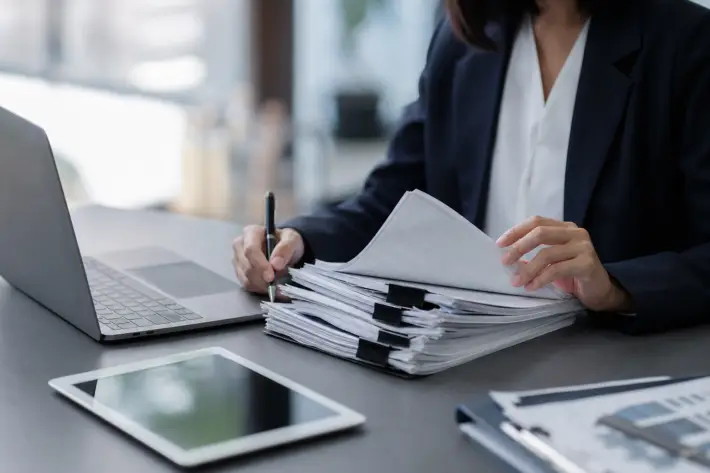 professional reviewing bulk job posting compliance documentation with pen, laptop, and tablet.